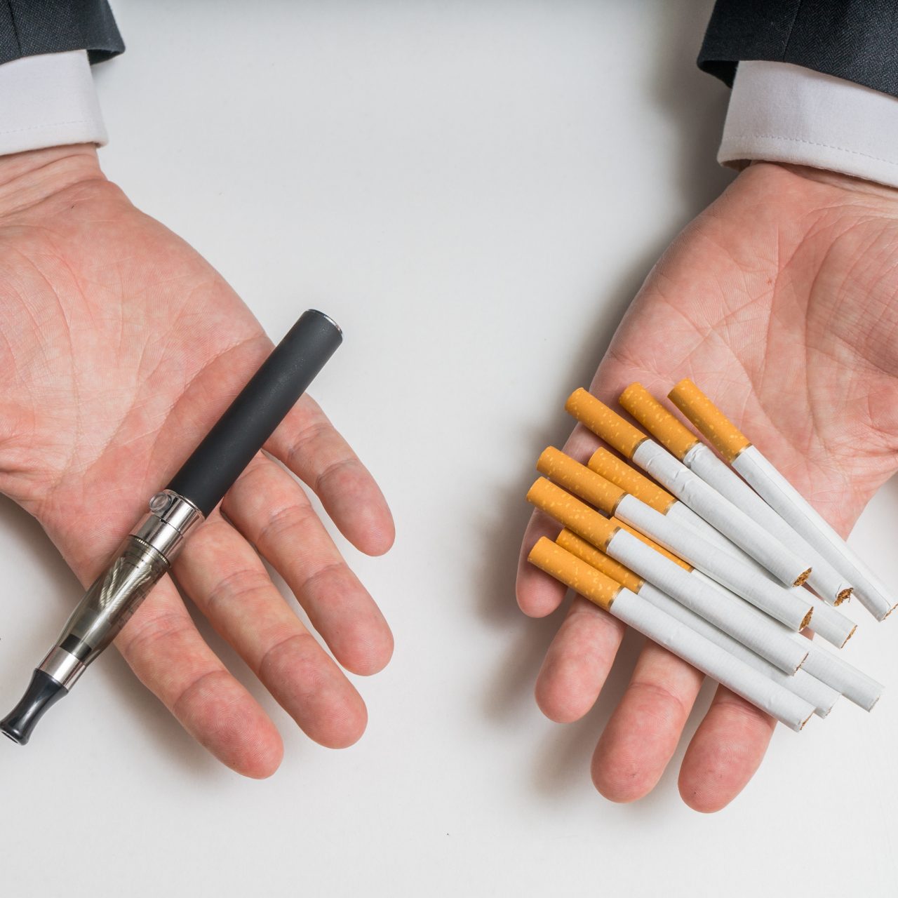 Hands holding electronic and conventional tobacco cigarettes and comparing. Hands are holding electronic vaporizer and conventional tobacco cigarettes and comparing them.